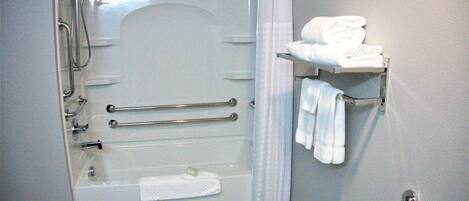 Ducha a pie con mampara de vidrio, toallero con toallas dobladas y barra de apoyo para mayor seguridad.