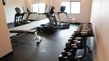 Een sportschool met loopbanden, een elliptische trainer en een bank.