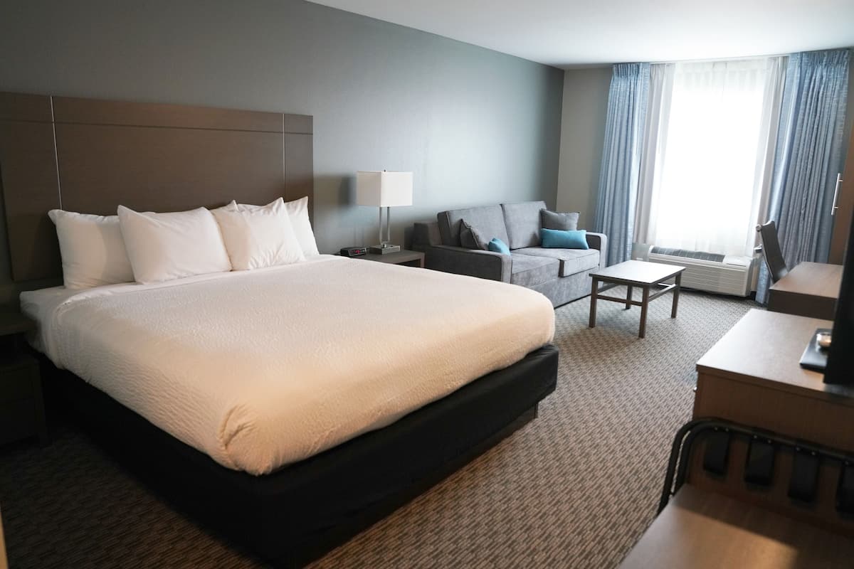 A hotel room with a large bed, a sofa, a small table, and a desk with a chair.