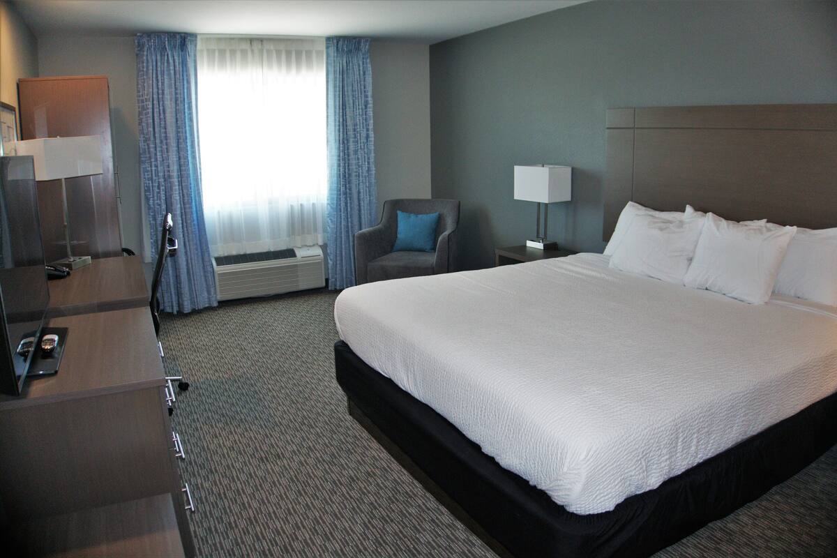 A hotel room with a large bed, a desk with a lamp, a chair, and a window with curtains.