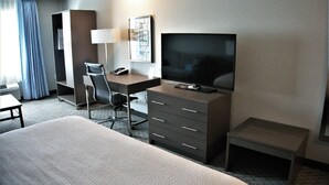 A hotel room with a bed, a desk with a chair, a television, a wardrobe, and a small table. - Brookstone Fort Dodge (Fort Dodge)