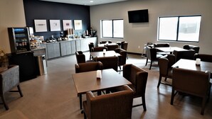 A modern dining area with multiple tables and chairs, a kitchen in the background, and large windows providing natural light. - Brookstone Fort Dodge (Fort Dodge)