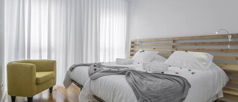 Quarto moderno com cama, cabeceira de madeira, poltrona amarela e uma janela grande com cortinas brancas.