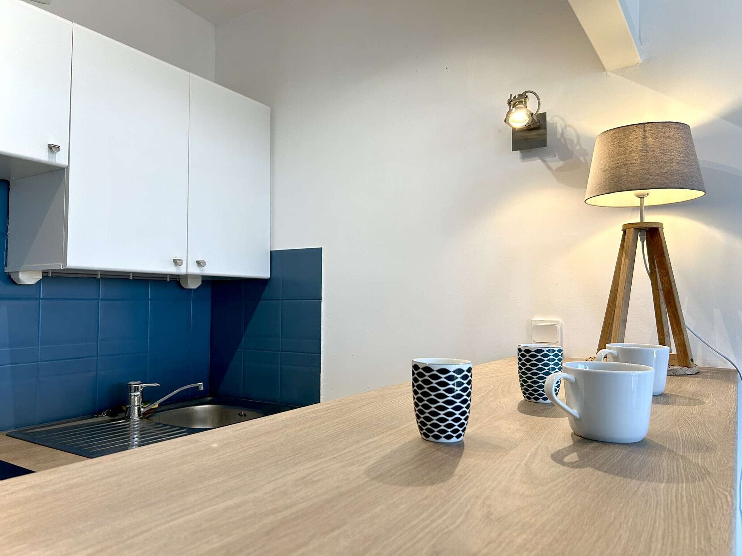 Eine moderne Küche mit weißen Schränken, einer blauen Spritzschutzwand, einer Holz Arbeitsplatte, einer Spüle und einer Lampe.
