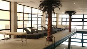 A sunlit indoor pool area with lounge chairs and palm trees. - Khazar Golden Beach (Baku)
