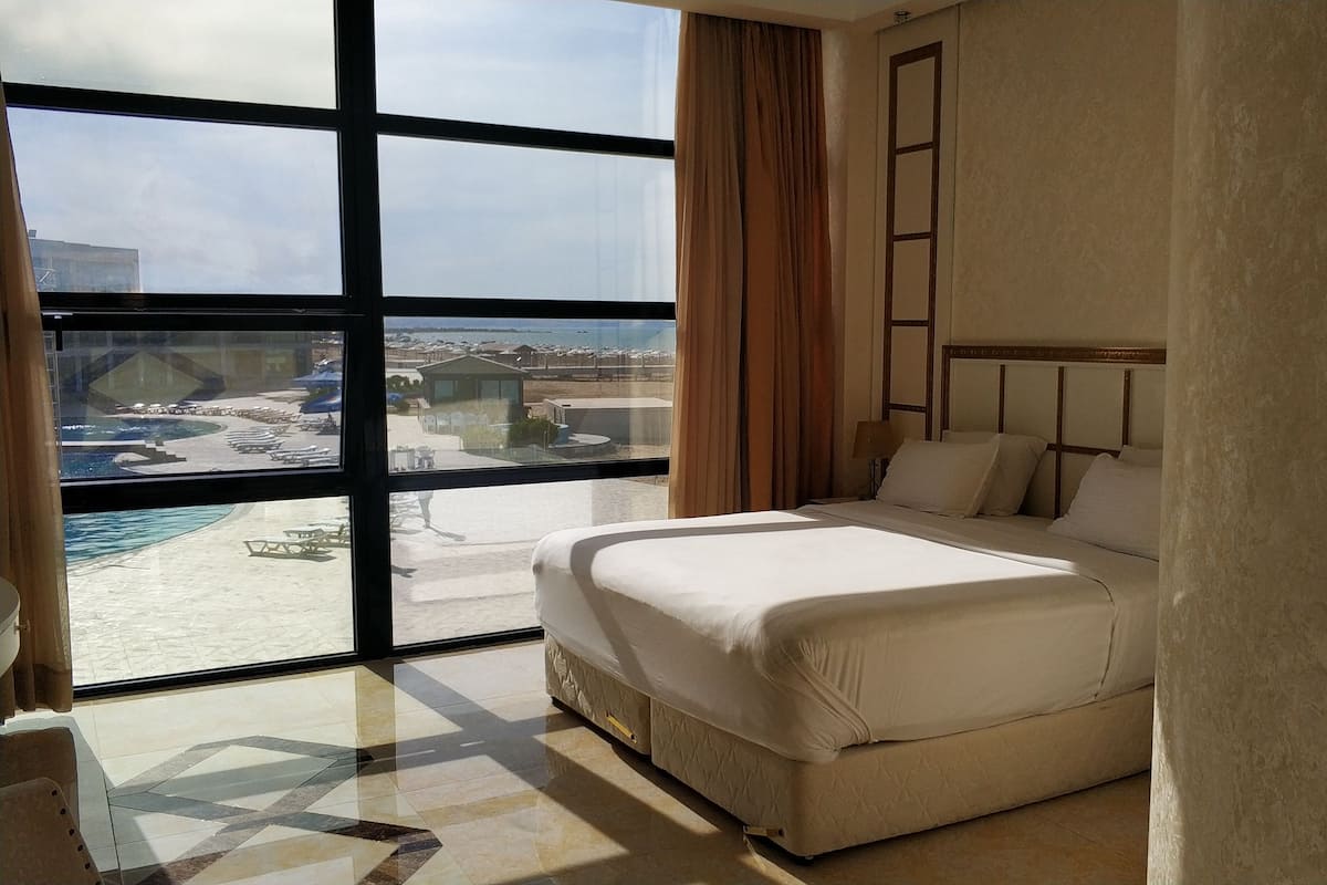 A hotel room with a large window, a bed, and a view of a pool and buildings.