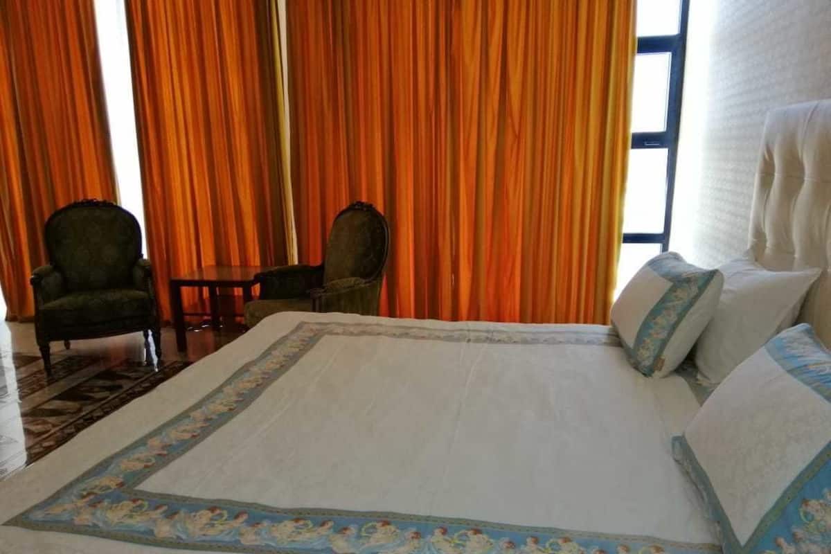 A hotel room with a large bed, two chairs, a small table, and a window with curtains.