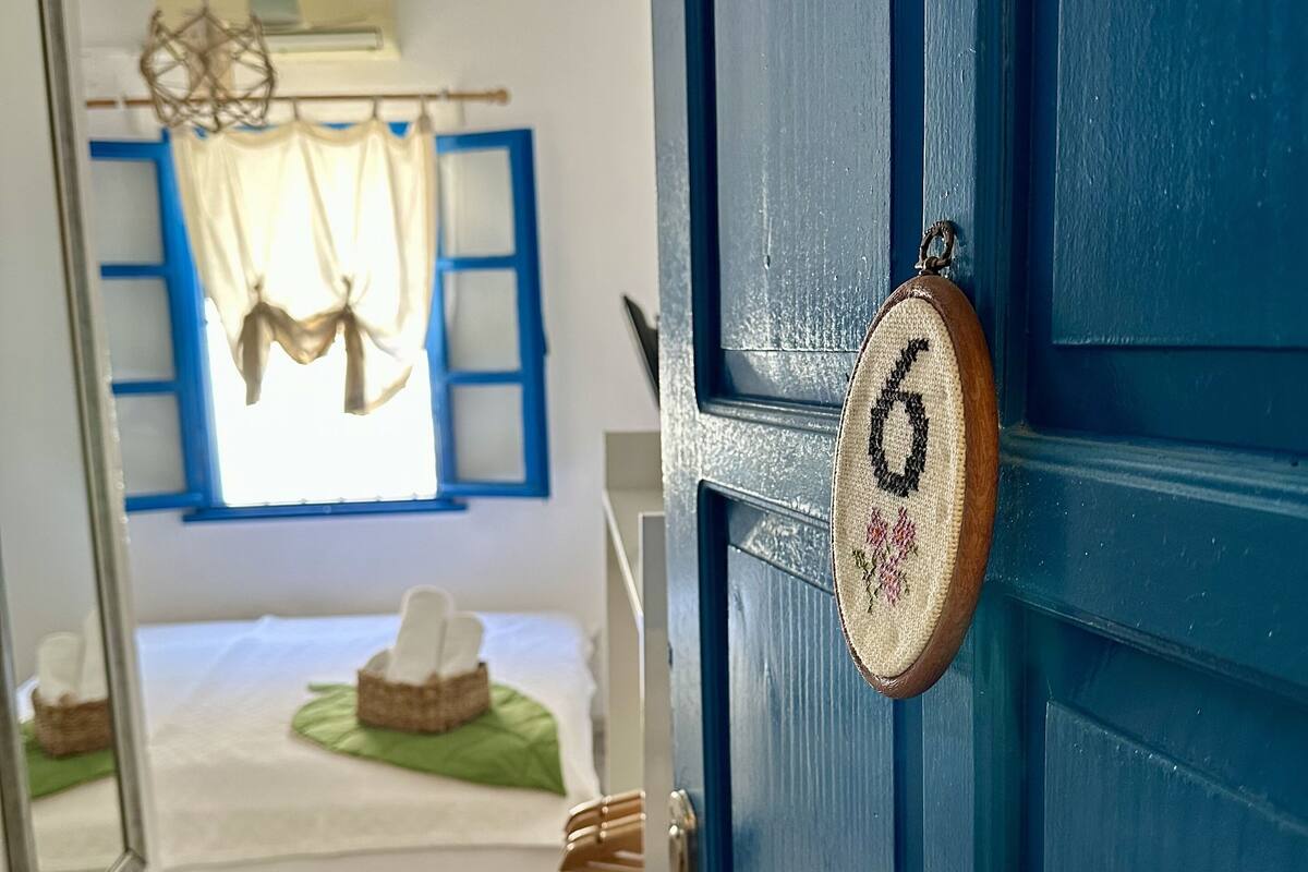 A room with a bed, a window with curtains, a hanging light fixture, and a door with a number lock.