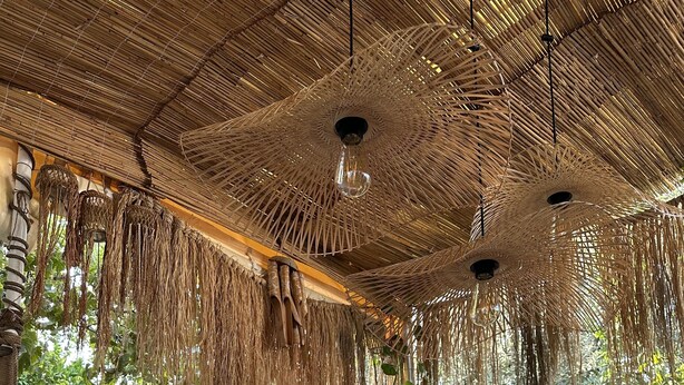 Un espace extérieur aménagé, abrité et doté d’un plafond en osier, de fauteuils confortables, d’une table avec des bougies et de plantes en pot.