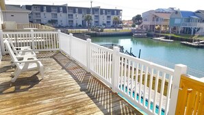 A wooden deck with white railings overlooking a marina with boats and buildings in the background.