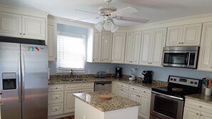 A kitchen with white cabinetry, a stainless steel refrigerator, a microwave, a stove, and a ceiling fan.