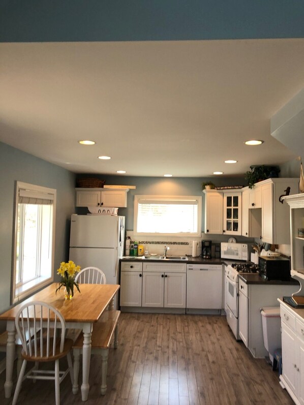 A compact kitchen with white cabinets, a wooden dining table, and a window providing natural light. - Steps away to sub sugar sandy beach - sleeps 6  (Caseville)