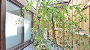 Un jardin japonais traditionnel avec une clôture en bambou, un sentier de pierres et un petit arbre.
