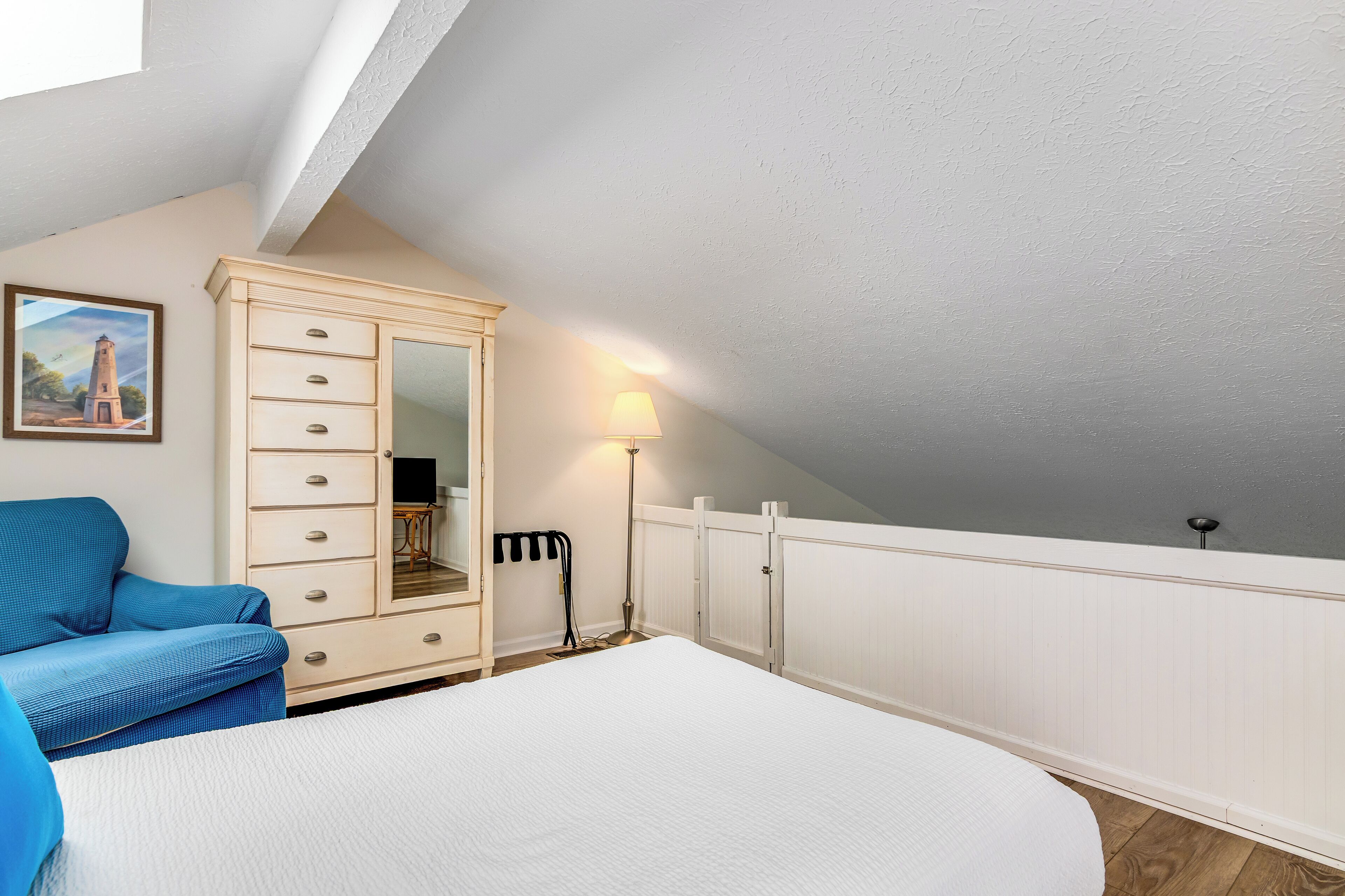 A bedroom with a bed, a dresser, a lamp, and a painting on the wall.