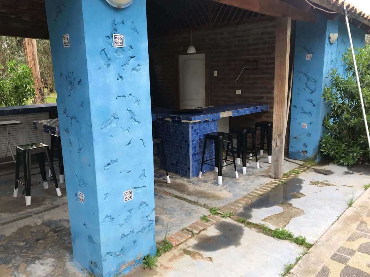 Un área de bar al aire libre con paredes de azulejos azules, taburetes negros y una barra.