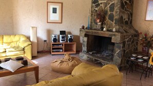 Una sala de estar acogedora con chimenea de piedra, un sofá amarillo, una mesita de centro y una pequeña mesa con libros.