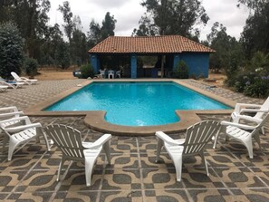 Una piscina con sillones de descanso y una zona techada.