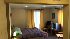 Una habitación pequeña y acogedora con cama, televisión, silla y lámpara.