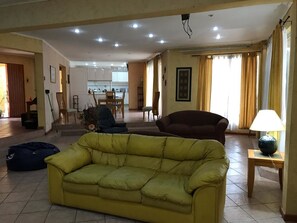 Una sala de estar con un sofá amarillo, un sillón de peluche azul, un sillón rojo y una lámpara sobre una mesita.