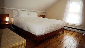 Ein Schlafzimmer mit einem hölzernen Bett, weißer Bettwäsche, einem Nachttisch mit Lampe und einem Fenster mit durchsichtigen Vorhängen.