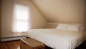 Ein Schlafzimmer mit einem großen Bett, Holzboden, einem Fenster mit Vorhängen und einer hölzernen Kommode.