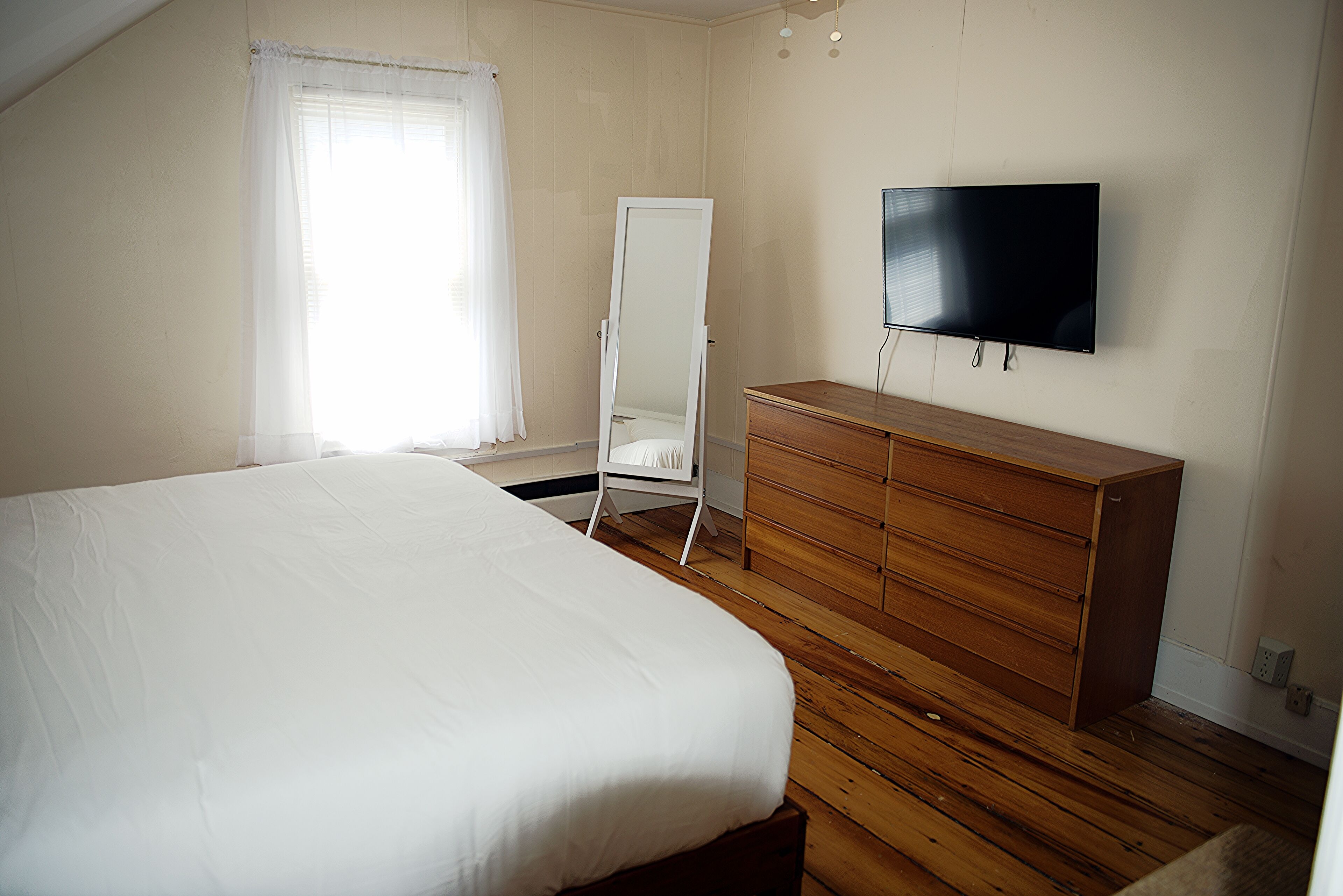 Ein Schlafzimmer mit einem Bett, einem Holzschrank, einem großen Spiegel und einem an der Wand montierten Fernseher.