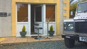 Un bâtiment avec une entrée de plain-pied, une chaise à l’extérieur et un Land Rover garé devant.