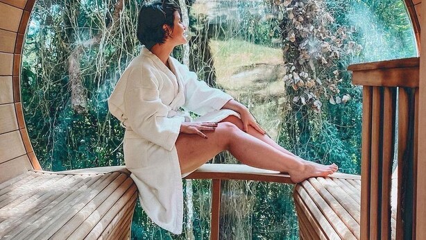 A person seated on a wooden bench inside a circular wooden structure with a view of a lush garden. - Confraria Colonial Hotel Boutique (Mairinque)