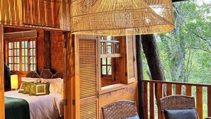 A wooden cabin bedroom with a bed, a window, and a balcony with wicker chairs. - Confraria Colonial Hotel Boutique (Mairinque)