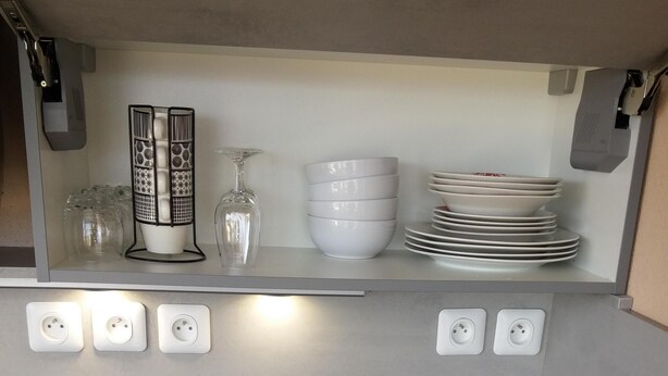 A kitchen with a black induction cooktop, white cabinets, and a shelf with stacked plates and a decorative item. - Spacious and cozy studio with breathtaking views (Saint-Mandrier-sur-Mer)