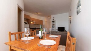 A dining area with a wooden table set for four, a bottle of wine, and a television in the background. - Cristianmar (Los Cristianos)
