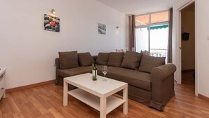 A living room with a brown sofa, a white coffee table, and a bottle of wine. There are two wall-mounted light fixtures and a window with a view. - Cristianmar (Los Cristianos)