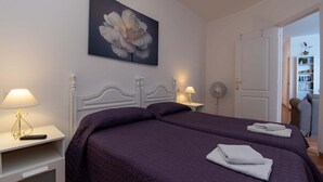 A bedroom with two beds, a large floral painting on the wall, bedside lamps, and a door leading to a bathroom. - Cristianmar (Los Cristianos)