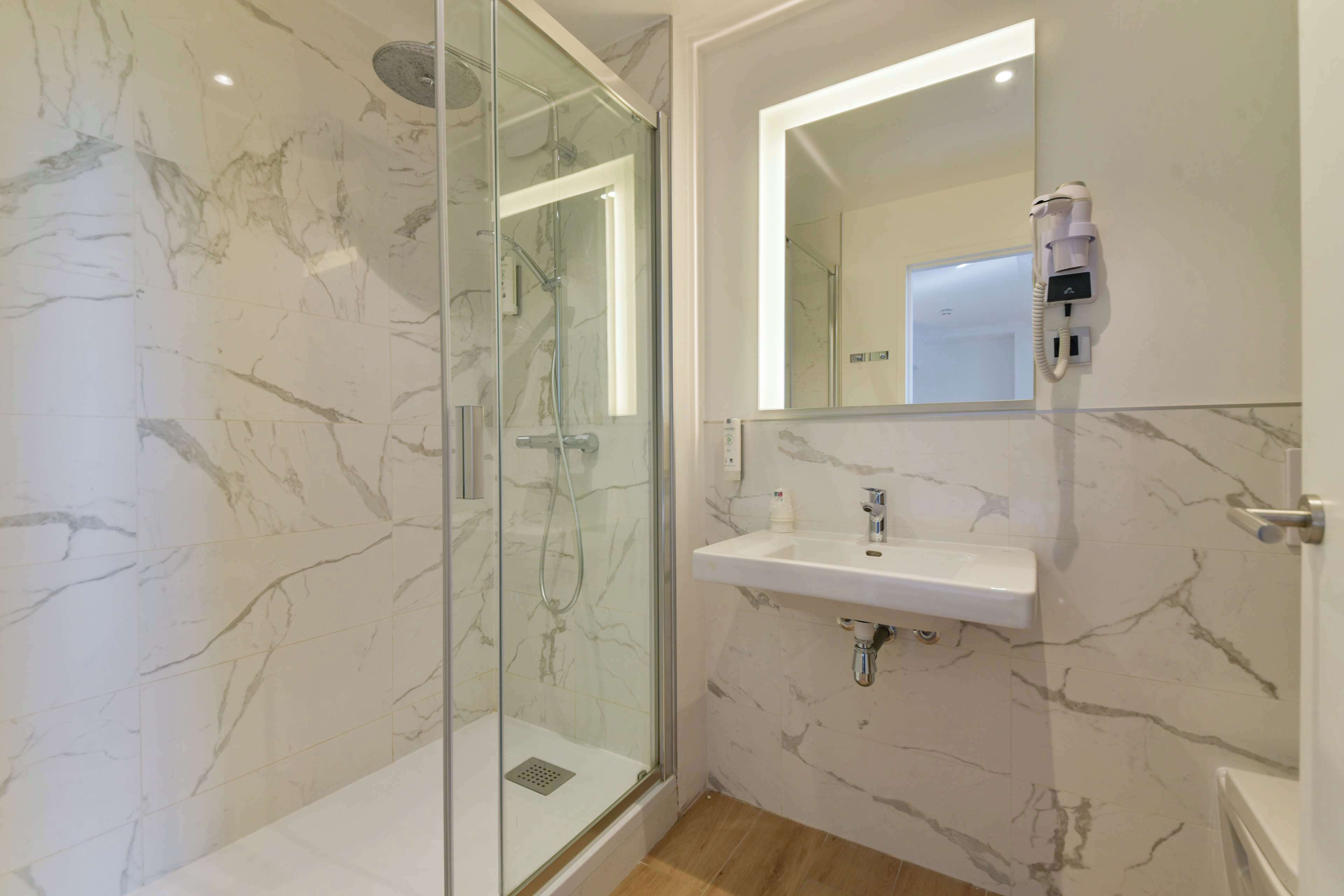 A modern bathroom with a glass-enclosed shower, a marble-tiled wall, a white sink, and a mounted phone.