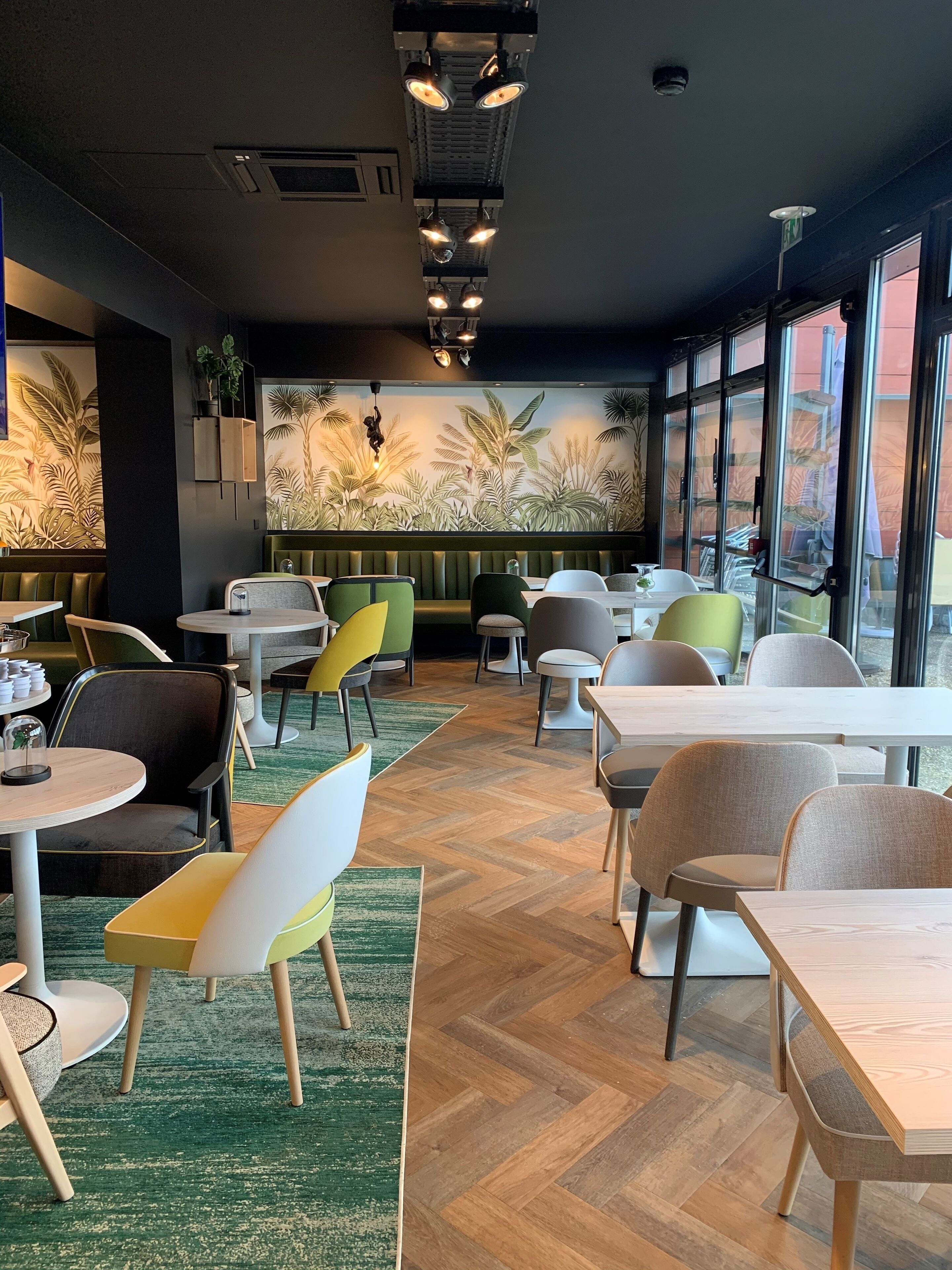 A restaurant interior with a tropical mural, green booths, and wooden flooring.