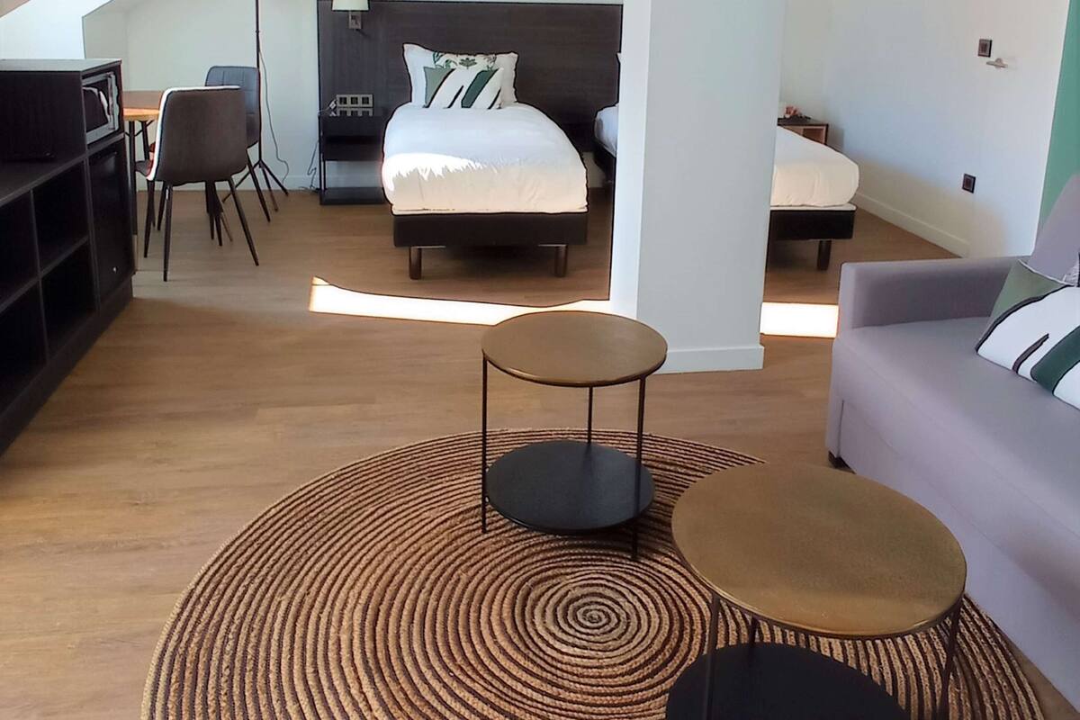 A modern loft-style bedroom with a large bed, a sofa, a coffee table, and a desk area with a chair.