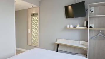 Una habitación de hotel moderna con una cama, un televisor montado en la pared, un escritorio con un portavasos y un espejo con diseño geométrico.