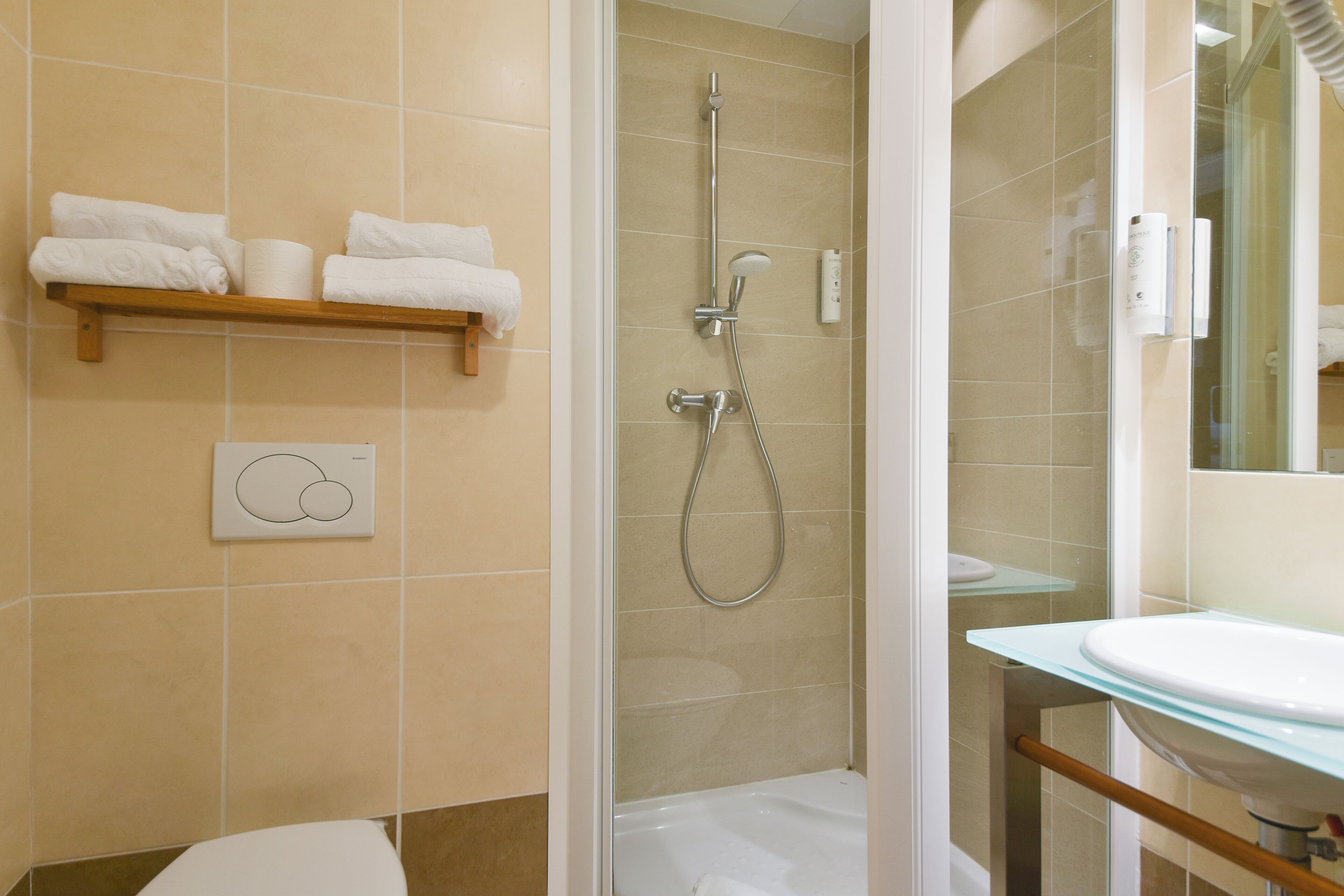 Un baño con ducha envuelta en vidrio, un lavamanos blanco y un perchero con toallas dobladas.