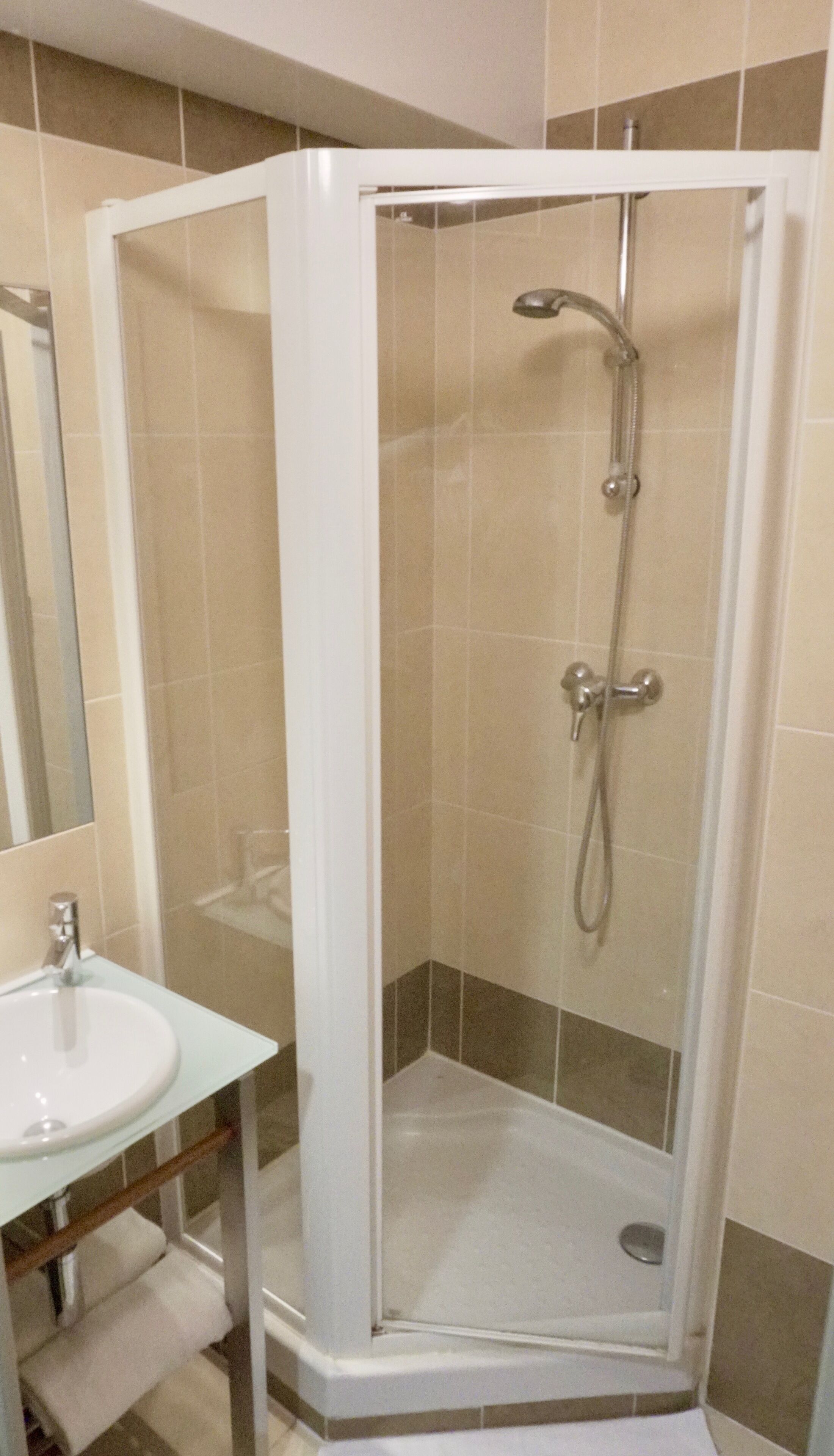 Cabina de bany amb envidriera, plat de dutxa amovible i aixeta fixa a la paret.