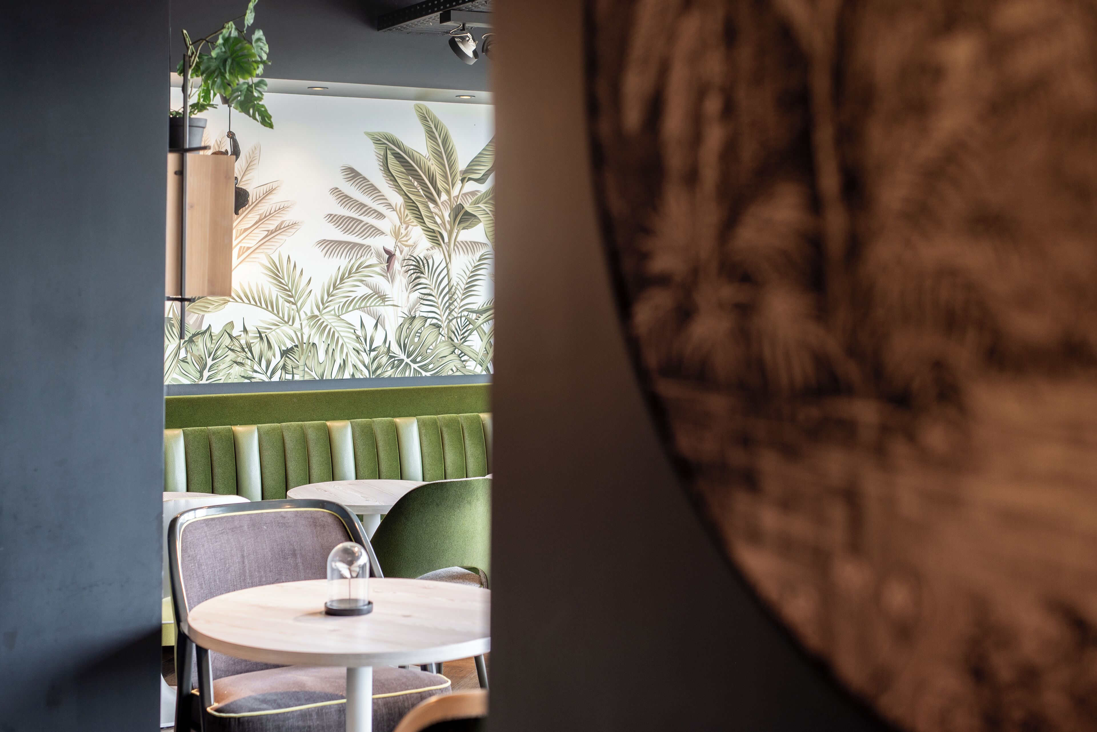 A restaurant interior with green booths, round tables, and a view of tropical plants.