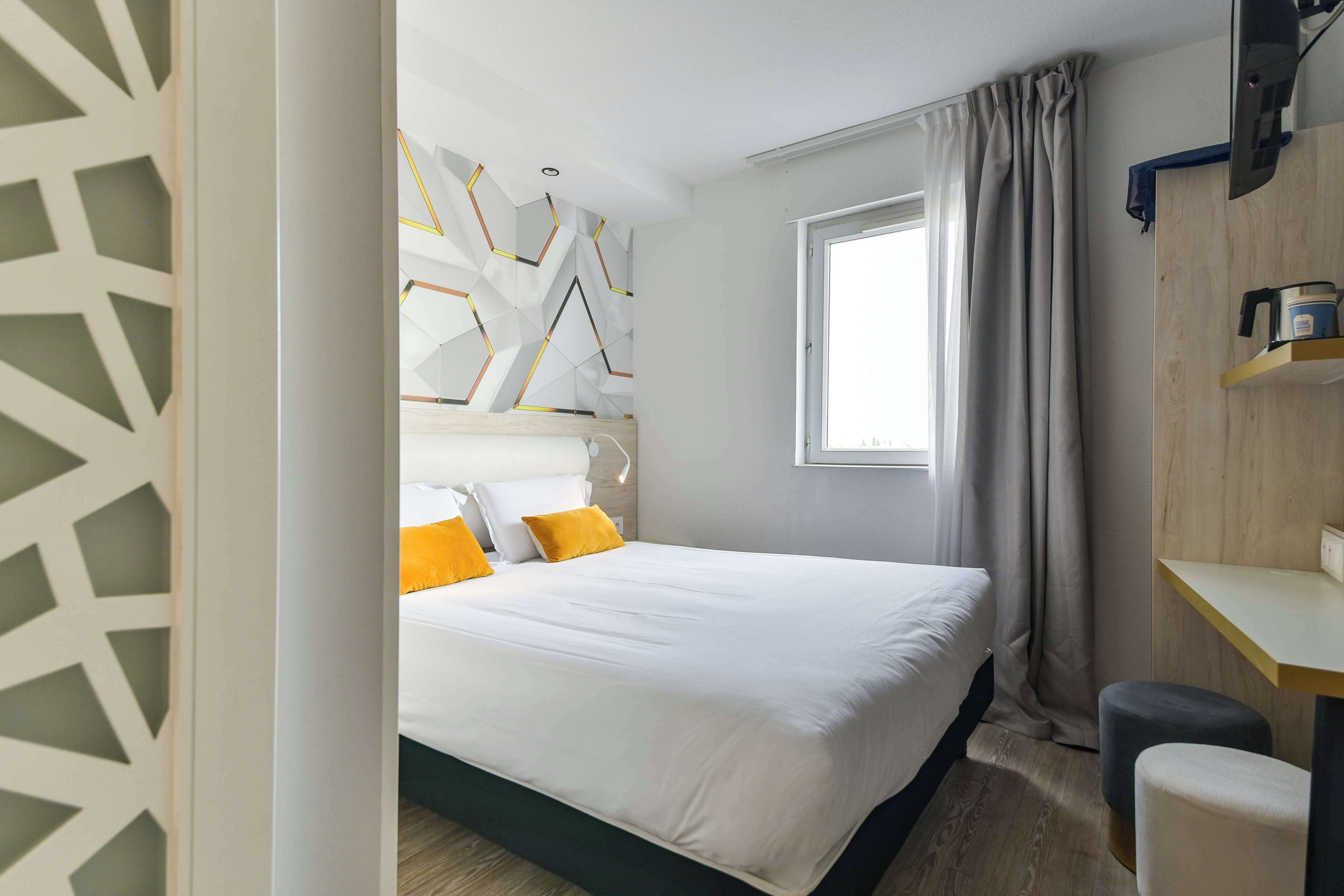 A modern hotel room with a large bed, a desk, and a window with curtains.