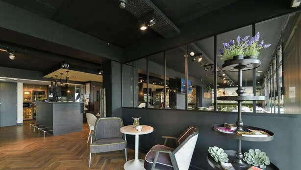 A modern interior with a bar area, seating, and a decorative plant stand. - Kyriad Crepy en Valois (Crepy-en-Valois)