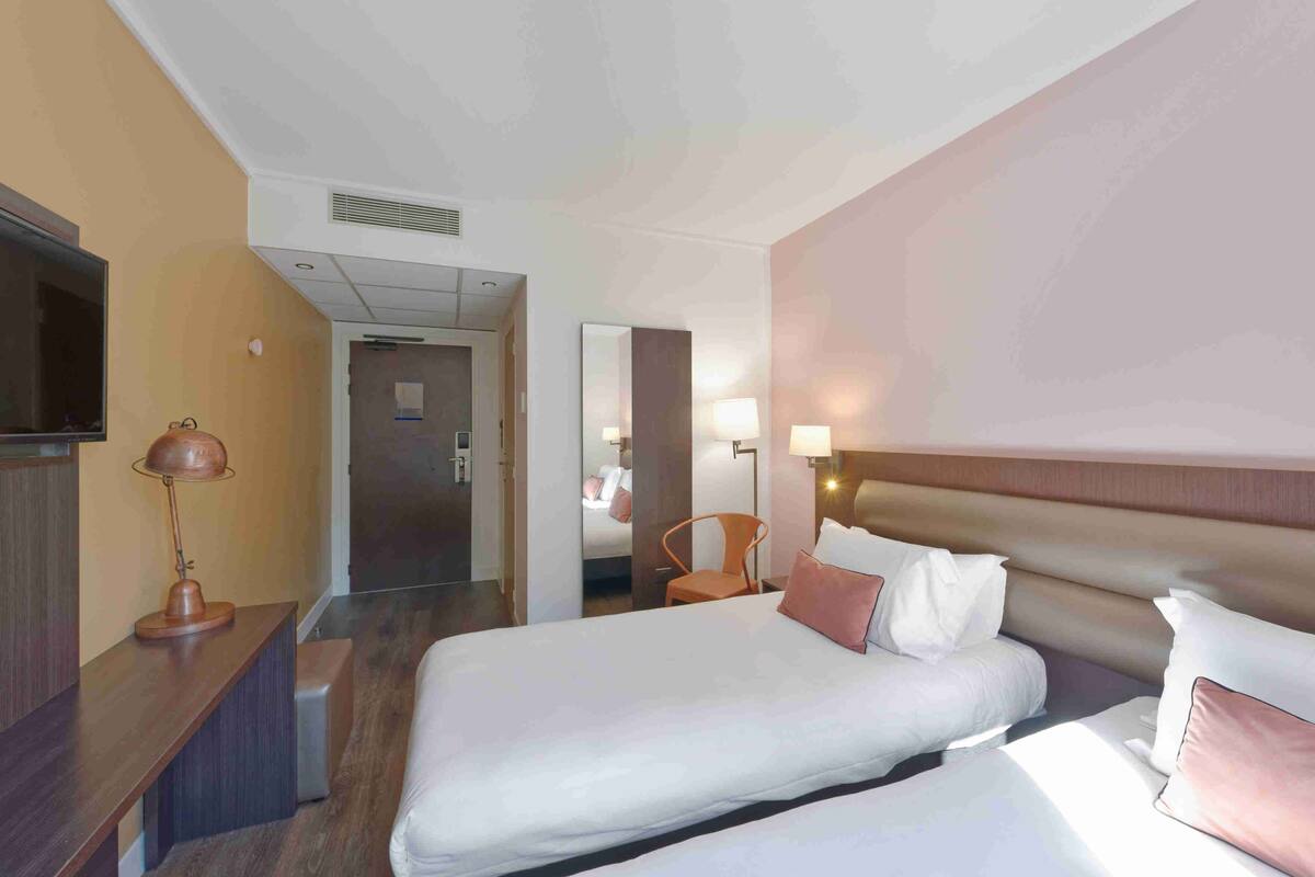 A hotel room with two beds, a TV, a desk, and a chair.