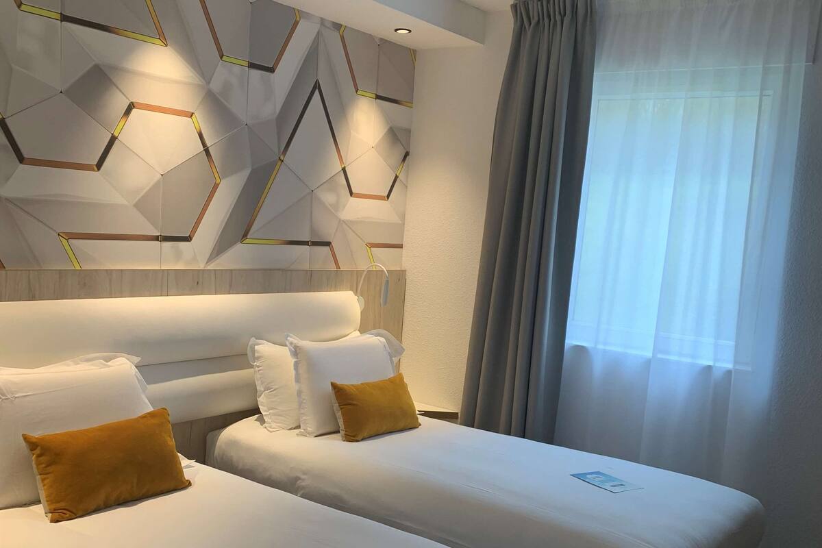 A hotel room with two beds, a modern geometric wall design, and a large window with curtains.