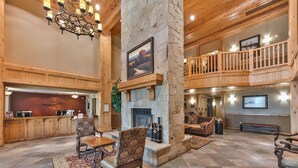 A spacious lobby with a stone fireplace, wooden furniture, and a balcony overlooking the interior.