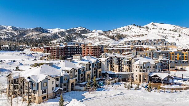 A snow-covered resort with multi-story buildings, ski slopes, and mountains in the background.
