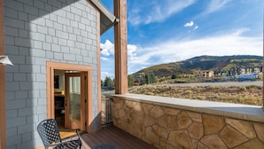 A balcony with a stone wall, a wooden door, and a view of a mountainous landscape.
