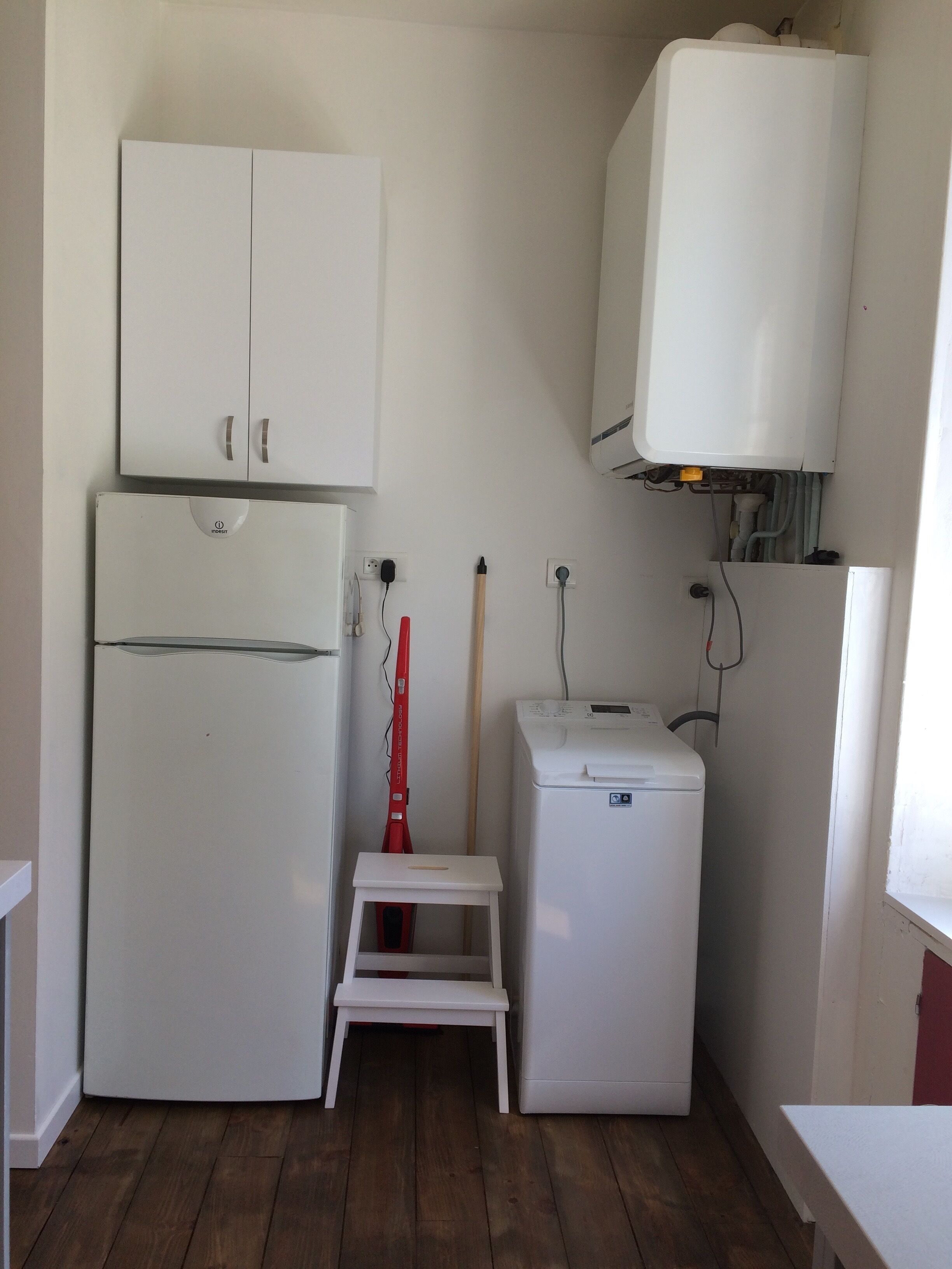 A compact kitchen with a refrigerator, a smaller appliance, and a step stool.