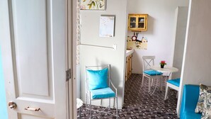 Een knus woongedeelte met een kitchenette, een eethoek met een kleine tafel en twee stoelen, een bank met blauwe kussens en een vloer met een patroon.