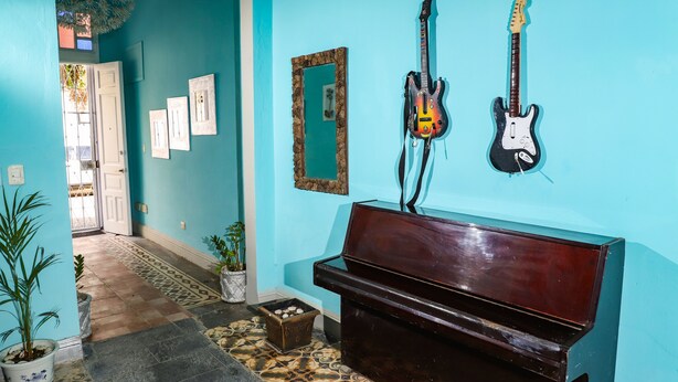 Een hal met een piano, twee gitaren, een spiegel en ingelijste foto’s aan de muur.